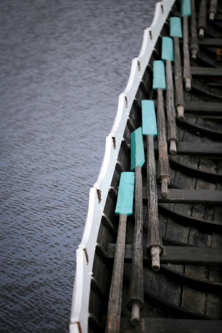 Oars resting along the side of a wooden Viking ship on the water